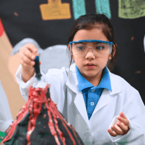 Niña del Colegio La Salle con bata blanca y lentes de protección realiza un experimento científico con un modelo de volcán en un ambiente escolar.
