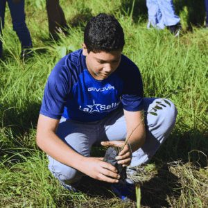 Estudiante del Colegio La Salle con camiseta azul siembra una planta en un área verde durante una actividad de cuidado ambiental.
