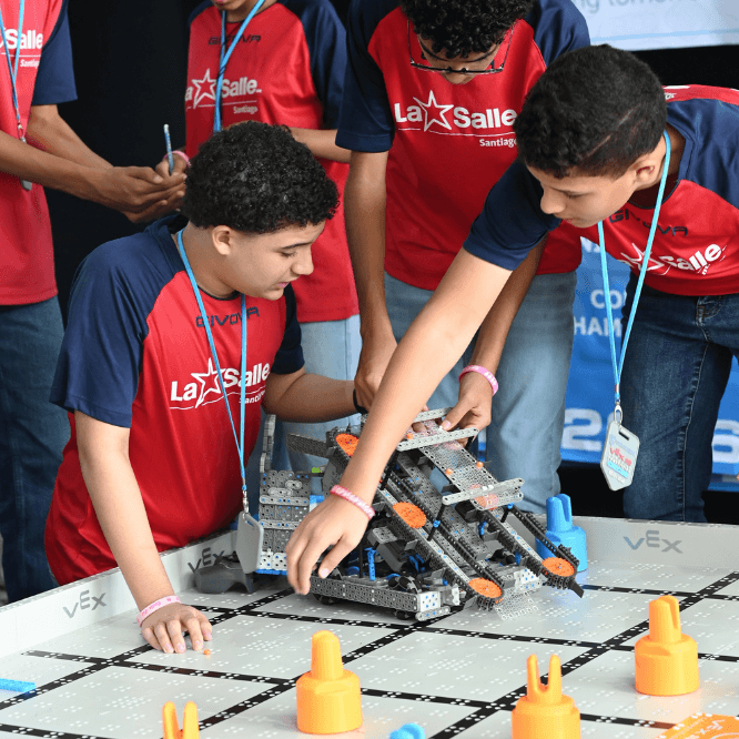 Grupo de estudiantes del Colegio La Salle con camisetas rojas participa en una competencia de robótica, manipulando un robot sobre una pista de desafíos VEX.