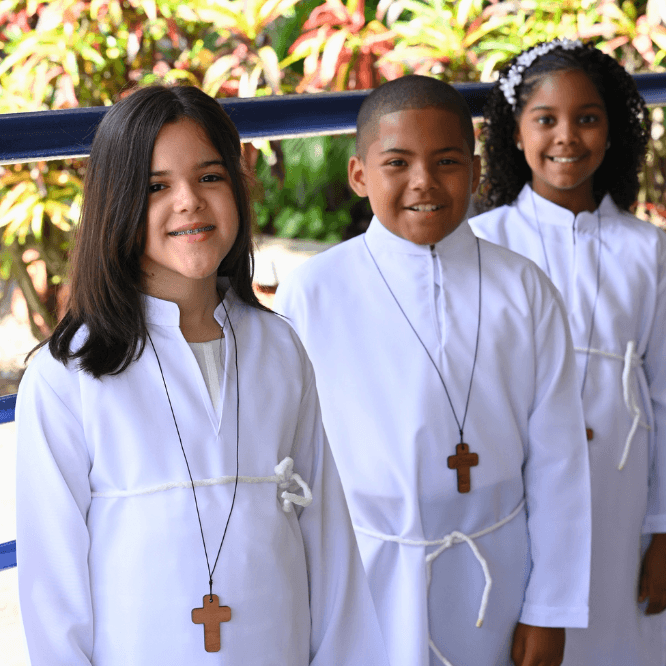Tres estudiantes del Colegio La Salle vestidos de blanco y con cruces de madera posan sonrientes durante una actividad religiosa escolar.