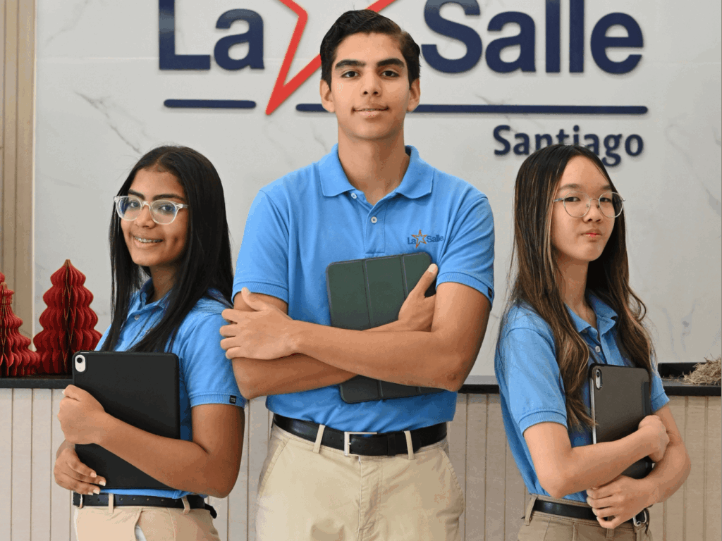 Tres estudiantes del Colegio La Salle con uniforme azul sostienen tablets frente al logo institucional de La Salle Santiago.